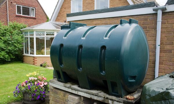 A large green plastic heating oil tank installed on a brick plinth in a garden beside a conservatory