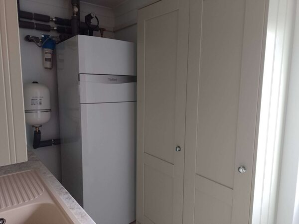 A Vaillant hot water cylinder installed in a utility room next to cream shaker-style cupboards, with pipework and an expansion vessel visible.