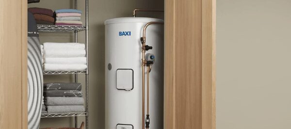 A white Baxi hot water cylinder installed in an airing cupboard next to shelving with folded towels