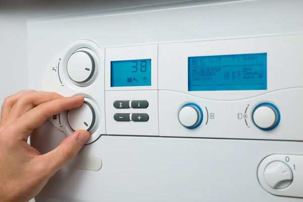 A hand turning a control dial on a white wall-mounted boiler with blue digital displays