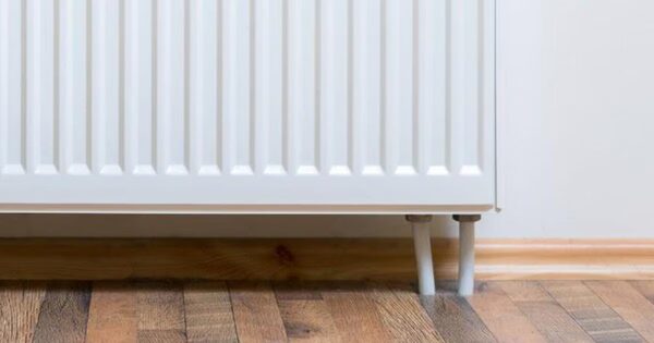 A white panel radiator mounted on a wall above a wooden floor