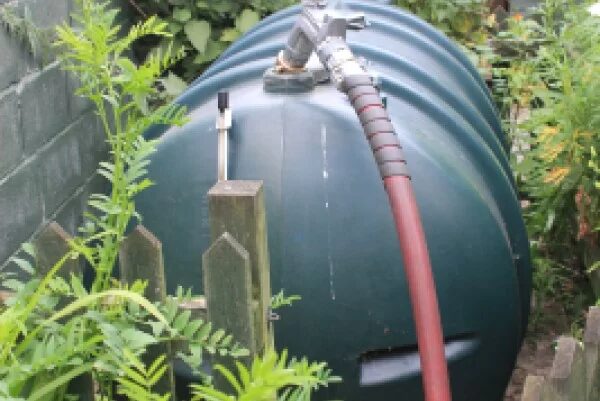 A green plastic domestic oil tank in a garden with a red delivery hose attached