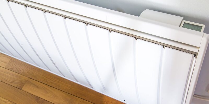A white electric panel heater with a digital control mounted on a wall above a wooden floor