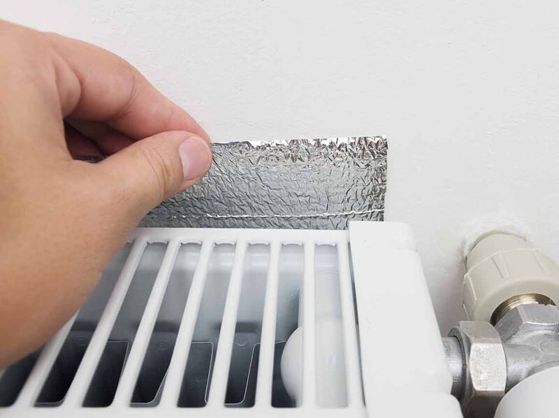 A hand placing a foil radiator reflector panel behind a white radiator