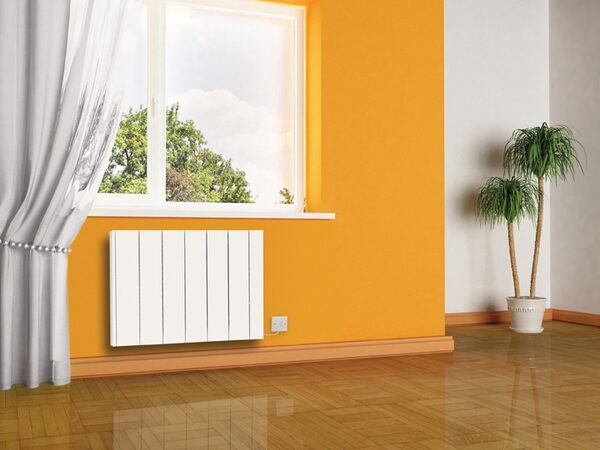A white electric radiator mounted on an orange wall beneath a window in a room with wooden flooring and a potted plant