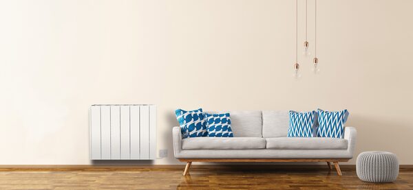 A white panel electric radiator mounted on a cream wall next to a grey sofa in a styled living room