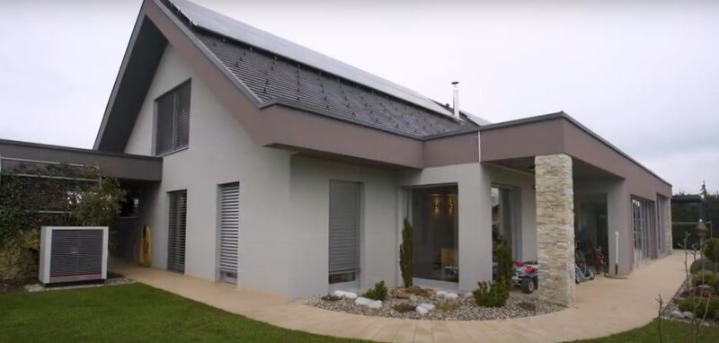 A modern house with solar panels on the roof and a heat pump unit beside it