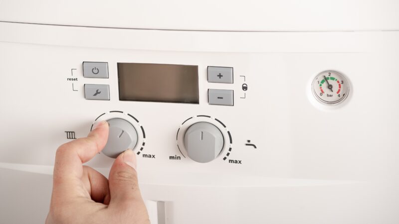 A hand turning a control knob on a white combi boiler's control panel with a pressure gauge and display