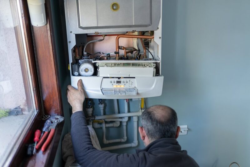 A heating engineer working on the open internals of a wall-mounted gas boiler in a home