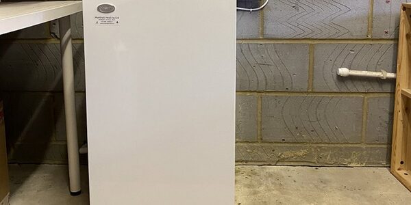 A white Grant oil boiler cabinet installed against a grey block wall in a utility space