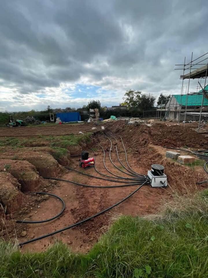 Ground source heat pump ground loop pipes being laid in a trench at a rural construction site