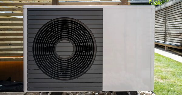 An air source heat pump unit installed outdoors in a garden next to a wooden fence