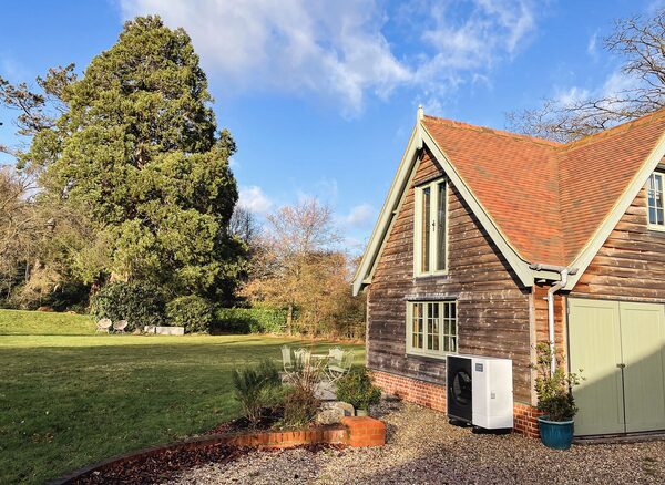 An air source heat pump unit installed outside a weatherboarded country house with a garden