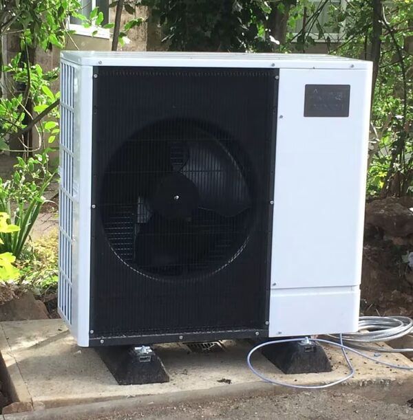 An outdoor air source heat pump unit installed on a concrete base in a garden