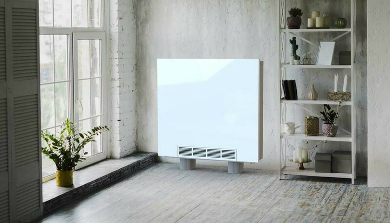 A white electric panel heater installed on the wall of a bright, minimalist room with a shelving unit and window