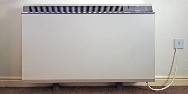 A white storage heater installed against an inside wall with a cable running to a wall socket
