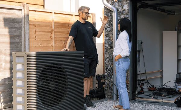 An installer talking to a woman beside an Aira air source heat pump installed outside a house