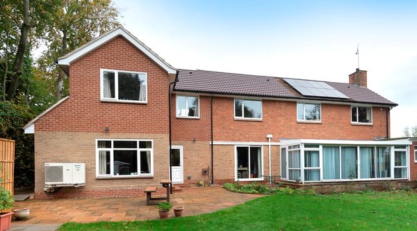A brick house with solar panels on the roof and an air source heat pump unit on the side wall