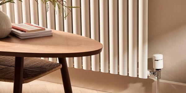 A white column radiator with a thermostatic radiator valve in a living room beside a wooden coffee table