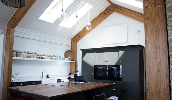 A white infrared heating panel mounted high on the wall of a vaulted timber-beamed kitchen