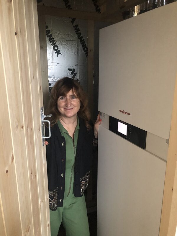 A woman standing beside a large white hot water cylinder in a timber-lined cupboard with foil insulation on the walls