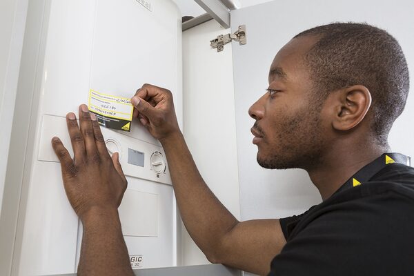 An engineer servicing a wall-mounted Ideal gas boiler, attaching a service label to the front panel