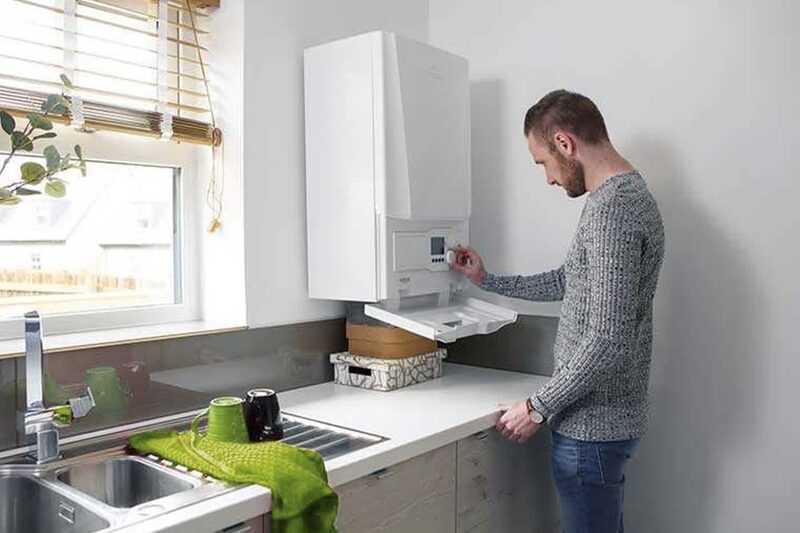 A man adjusting the controls of a white wall-mounted Ideal boiler in a kitchen