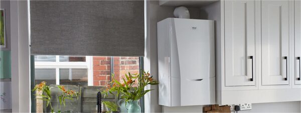 A white Ideal wall-mounted combi boiler installed in a kitchen above a worktop next to white cabinets and a window with flowers