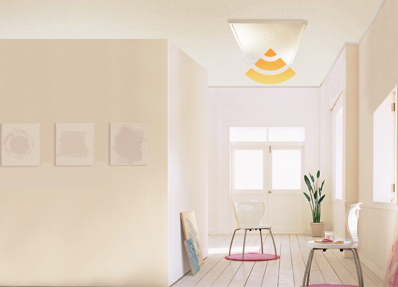 A white infrared heating panel mounted on the ceiling of a bright cream-coloured room with chairs and a plant, with an orange heat-wave graphic overlaid
