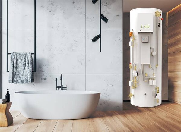 A white Joule branded hot water cylinder with exposed pipework and valves standing in a modern bathroom beside a freestanding bath