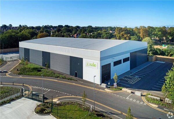 Aerial view of a large industrial warehouse building with Joule branding on the wall, surrounded by roads, car park and trees