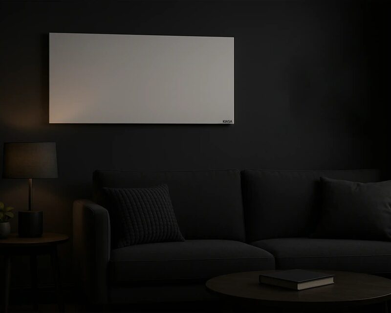 A white Kiasa infrared heating panel mounted on a dark wall above a black sofa in a dimly lit living room