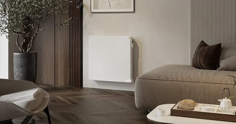 A white Myson electric radiator mounted on the wall of a modern living room with a sofa and potted tree