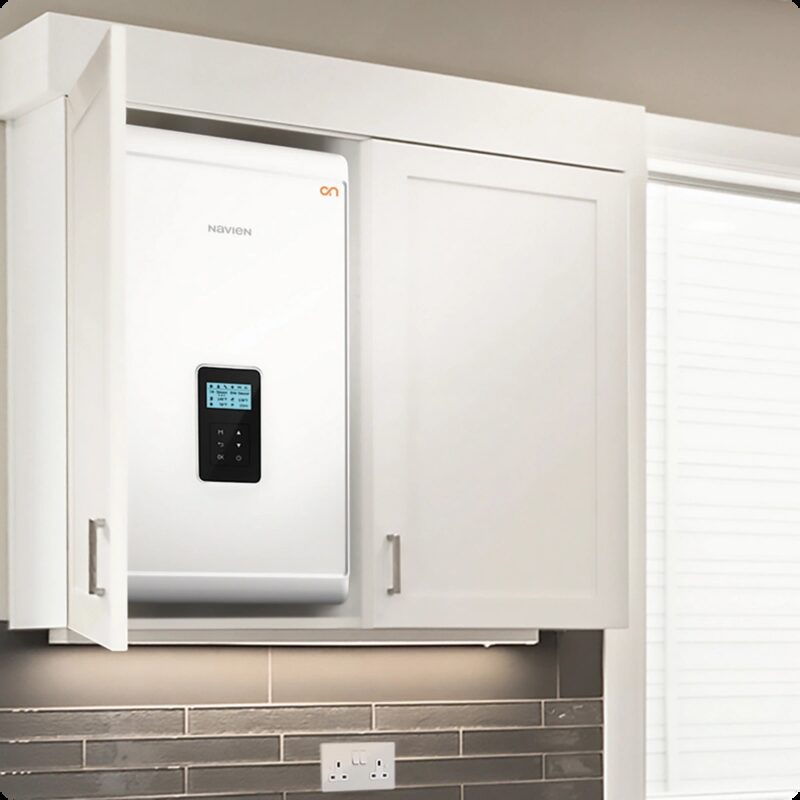 A white Navien wall-mounted boiler installed inside an open kitchen cupboard above a tiled worktop