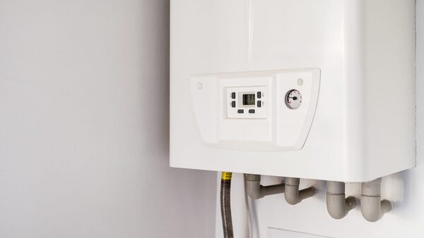A white wall-mounted gas combi boiler with digital display and pressure gauge, with copper and plastic pipes below