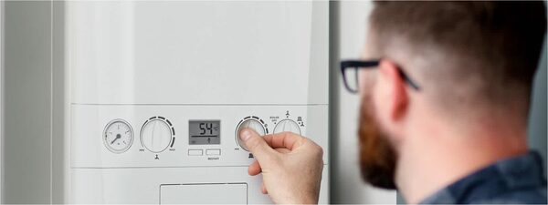 A man adjusting the control dial on a white wall-mounted Ideal boiler
