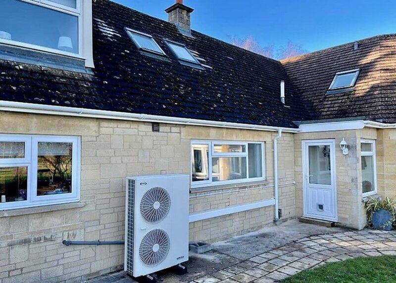An air source heat pump unit installed on the exterior wall of a stone house