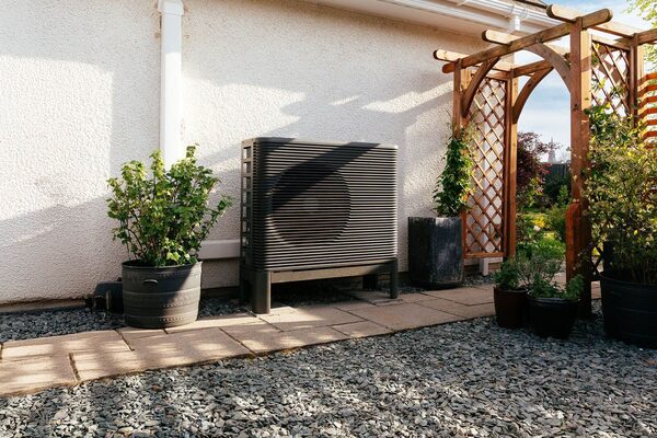 An Aira air source heat pump unit installed outside a house wall beside a gravel path and potted plants