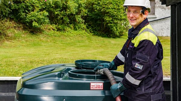 A delivery driver in high-visibility workwear and hard hat filling a green domestic heating oil tank with a hose