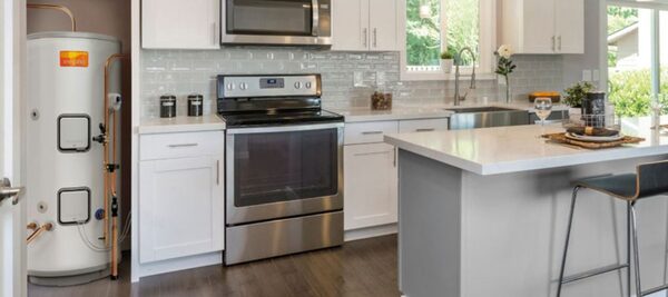 A white Megaflo hot water cylinder installed in a utility space next to a modern white kitchen with a stainless steel range cooker