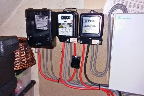 A Radio Teleswitch Service meter and two electricity meters mounted on a wall with red and grey wiring, next to a Vycker consumer unit