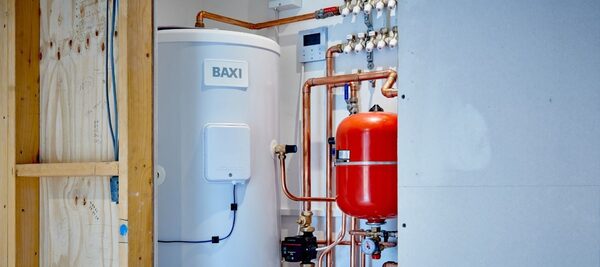 A white Baxi hot water cylinder installed in an airing cupboard with copper pipework, a red expansion vessel and manifold controls