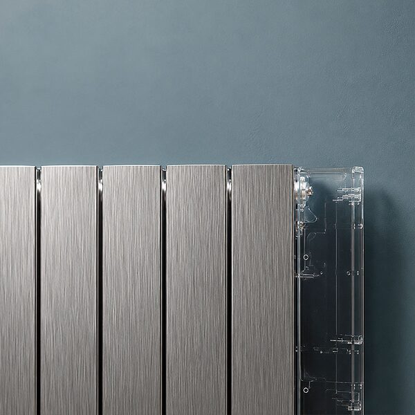 Close-up of a brushed aluminium electric radiator panel against a blue-grey wall, with its clear plastic side casing partly open
