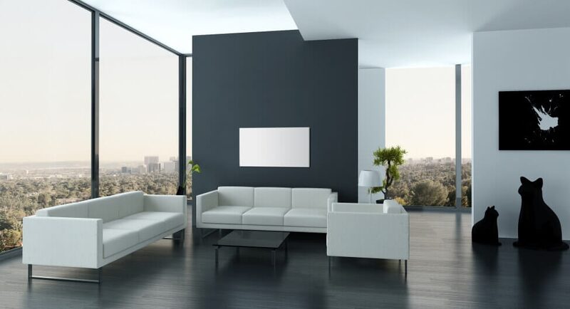 A white Sundirect infrared heating panel mounted on a dark wall in a modern minimalist living room with white sofas