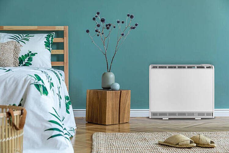 A white Sunhouse electronic storage heater standing against a teal wall in a styled bedroom