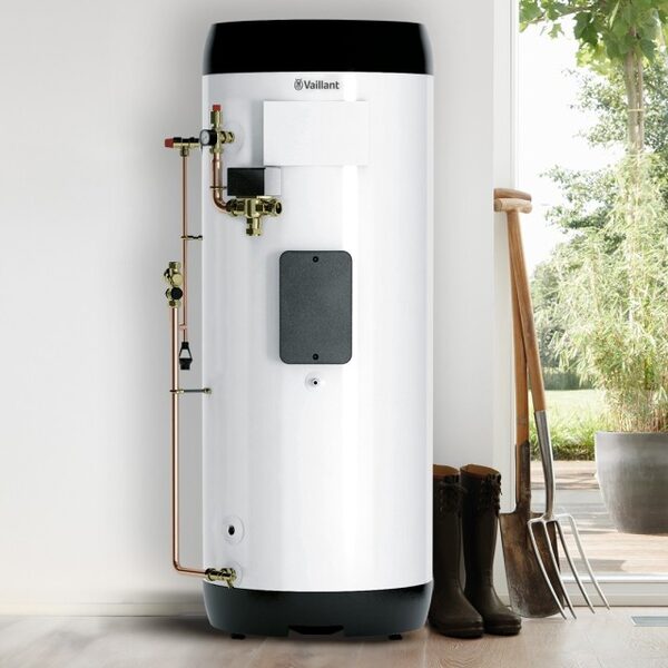 A white Vaillant hot water cylinder with copper pipework standing indoors next to wellies and garden tools by a door