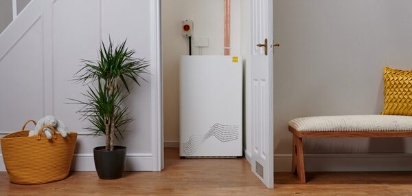 A white tepeo ZEB heat battery boiler installed in a home hallway next to a door, with a plant and bench nearby