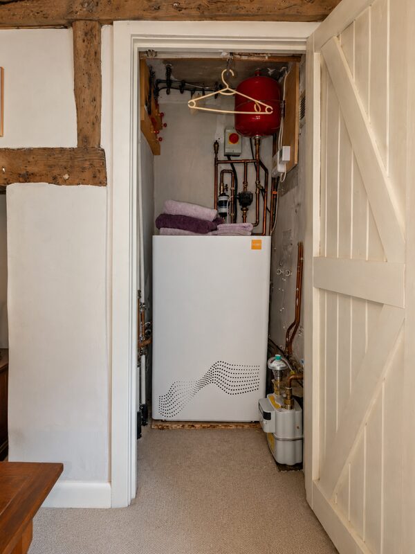 A tepeo Zero Emission Boiler (ZEB) installed in a small airing cupboard with copper pipework, expansion vessel and towels on top
