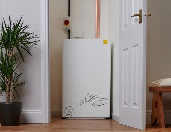 A white Tepeo Zero Emission Boiler heat battery unit installed in a hallway next to an open door, with copper pipework and an isolation switch above