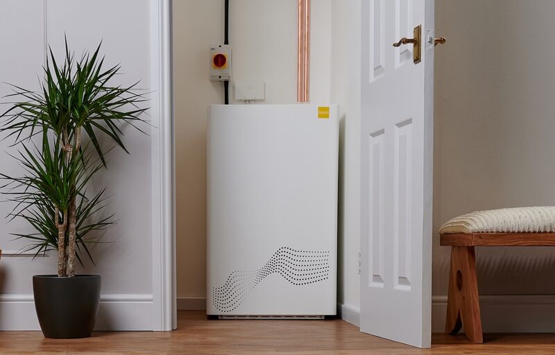 A white tepeo ZEB electric boiler installed in a hallway next to a plant and copper pipework
